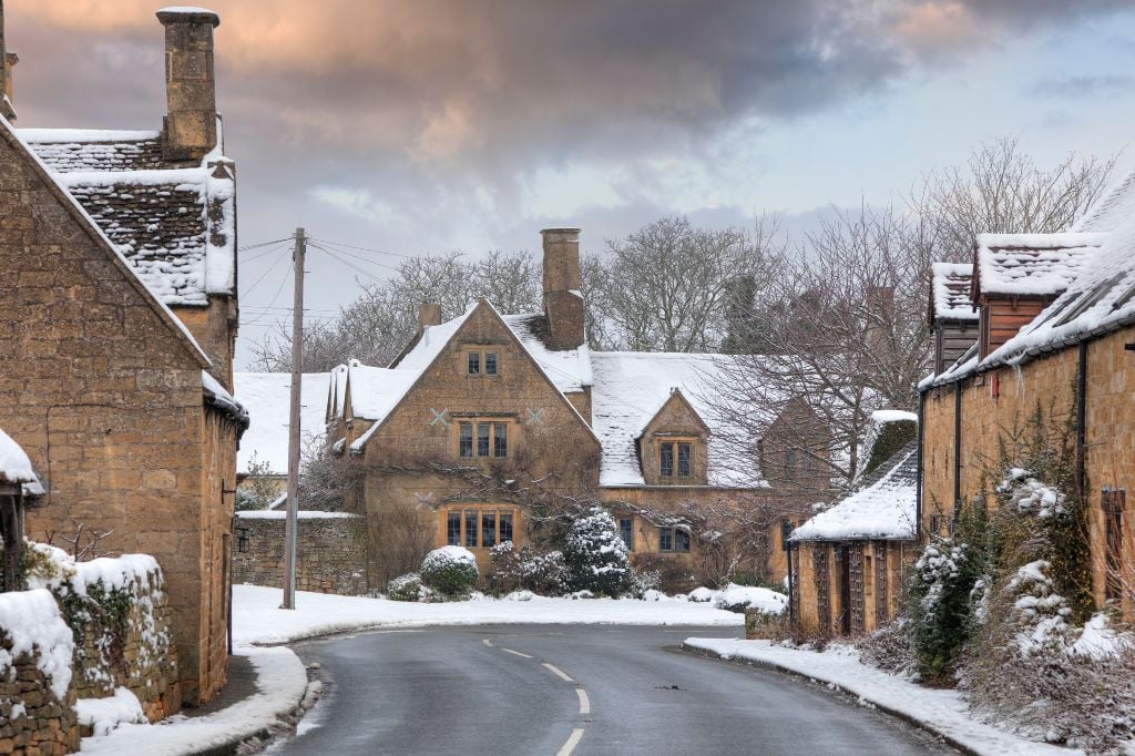 Snow-covered road through the Cotswolds countryside